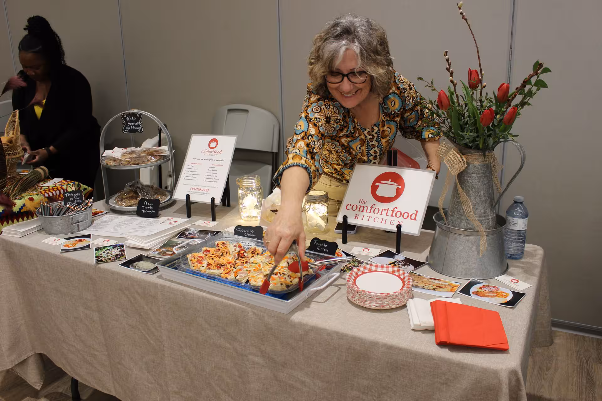 Food vendor speaking with attendees beside a product display.